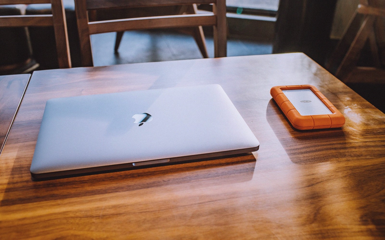 Closed laptop and orange portable hard drive on a wooden table
